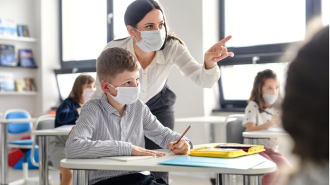 Un insegnate con la mascherina aiuta un suo alunno